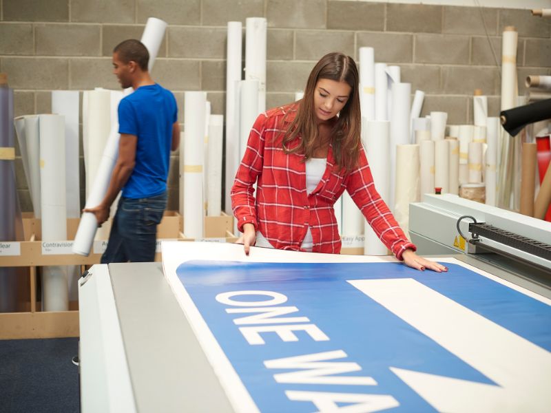 ragazza lavora in azienda sta stendendo dei cartelloni su un banco lavoro